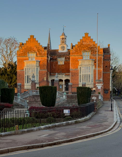 A modern residential street in Harrow Weald featuring multi-story brick buildings with black accents and large windows, under a bright blue sky with scattered white clouds. In the foreground, a paved